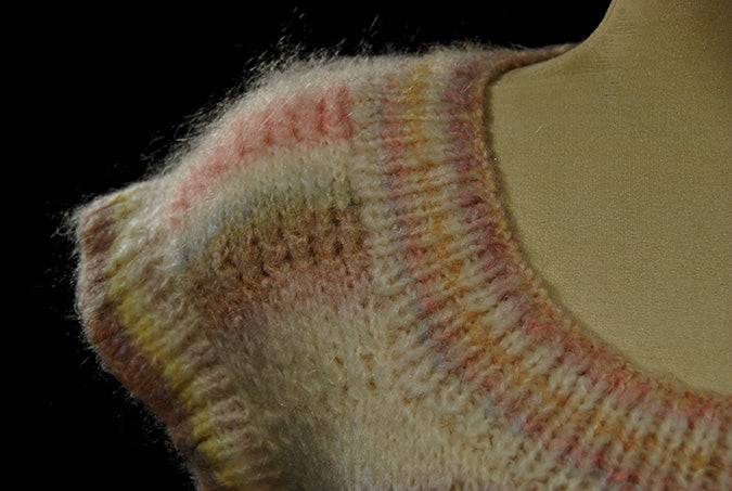 Close-up of a hand-knit woman's or girl's pastel-colored sleeveless sweater vest with round neck in spring and summer style