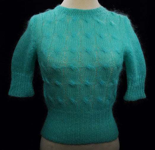 Girl's pale-green short-sleeve mohair sweater with cable knit pattern and crewneck design.