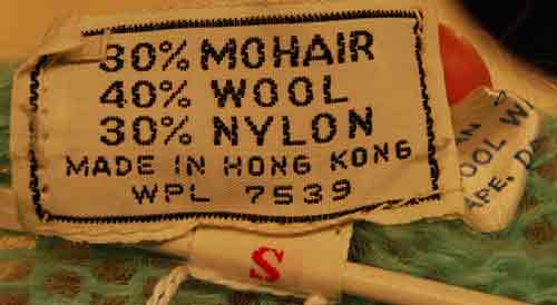 Close-up of a clothing label showing fabric composition of 30% mohair, 40% wool, 30% nylon, made in Hong Kong for a girl's pale-green short-sleeve mohair sweater.