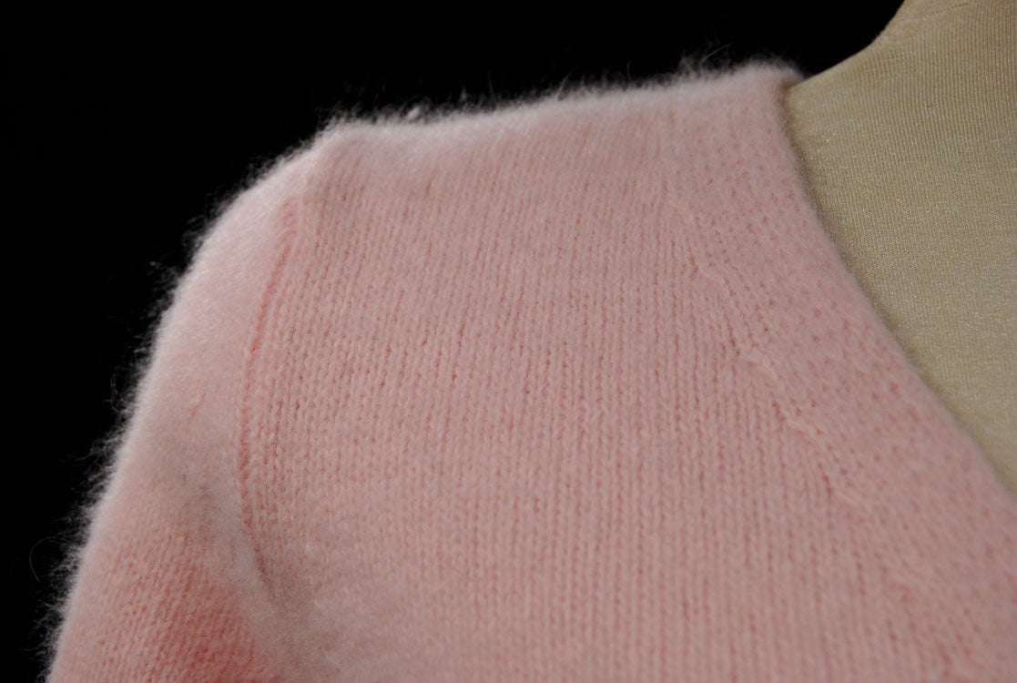 Close-up of woman's pink angora-lambswool crossover pullover sweater with soft texture and side button detail