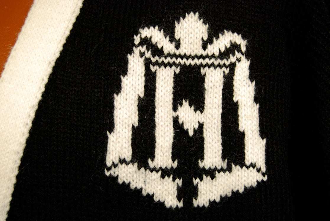 Close-up of woman's black with white trim cardigan tennis sweater featuring a white patterned tennis racket design.