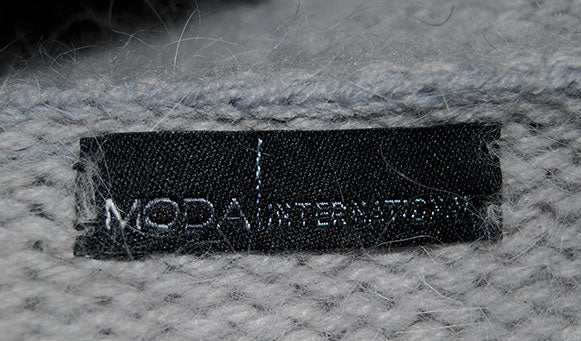 Close-up of black Moda International label on soft gray angora fabric of woman's angora shrug cardigan sweater