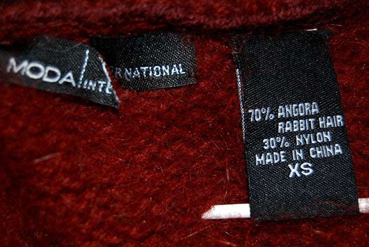 Close-up of a maroon Woman's Angora Shrug cardigan label showing 70% angora rabbit hair and 30% nylon composition, size XS.