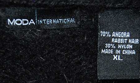 Close-up of Woman's Angora Shrug label showing 70% angora rabbit hair and 30% nylon blend, size XL by Moda International for Victoria Secrets