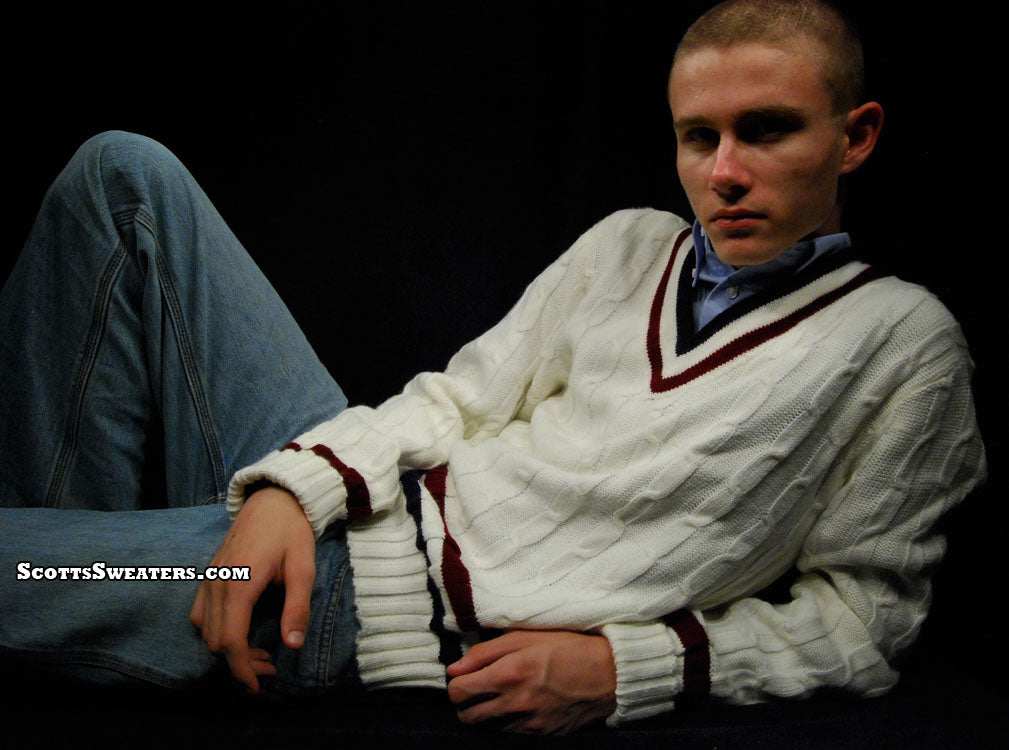 Men's classic V-neck cable-knit white tennis sweater with maroon trim modeled by a man reclining against black background