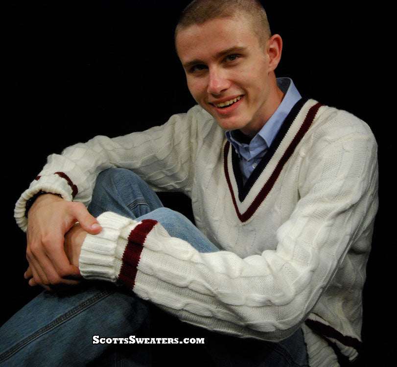 Men's classic V-neck cable-knit tennis sweater in white with maroon stripes, worn by smiling man sitting cross-legged