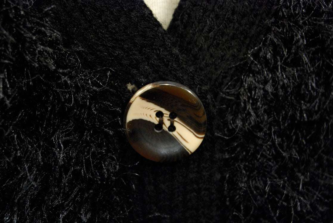 Close-up of black woman's eyelash cardigan sweater with shiny four-hole button and fuzzy acrylic fibers resembling rabbit fur
