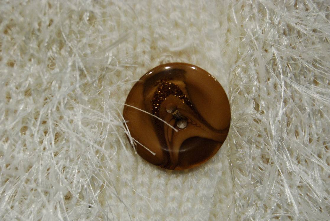 Close-up of brown button on white fuzzy eyelash cardigan sweater with long acrylic fibers