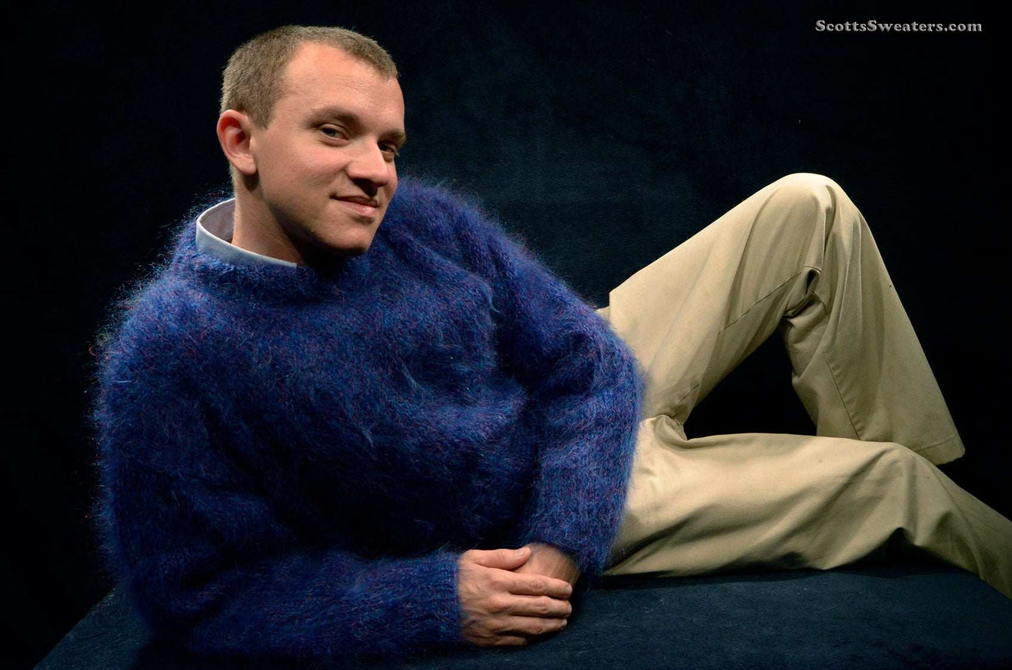 Man wearing navy-blue Scottish mohair men's crewneck sweater by Lairds of Scotland reclining against dark background