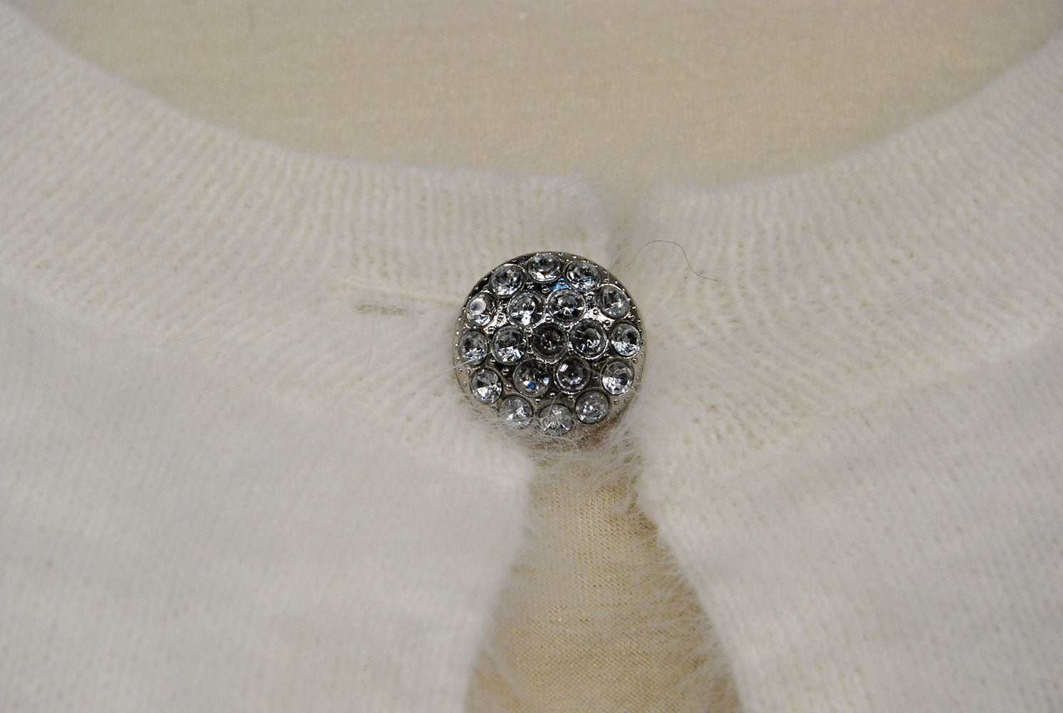 Close-up of jeweled rhinestone button on woman's white angora shrug cardigan sweater by Express
