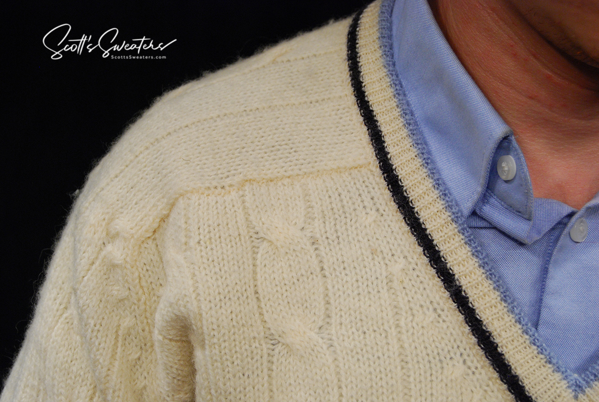 Retro classic ivory wool cable-knit tennis sweater with navy and French blue striped trim on V-neck, worn over a blue collared shirt.