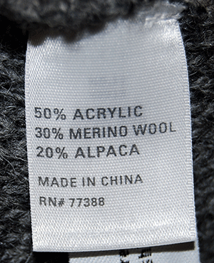Tag showing fabric composition of woman's grey alpaca-merino wool sweaterdress with 50% acrylic, 30% merino wool, and 20% alpaca.