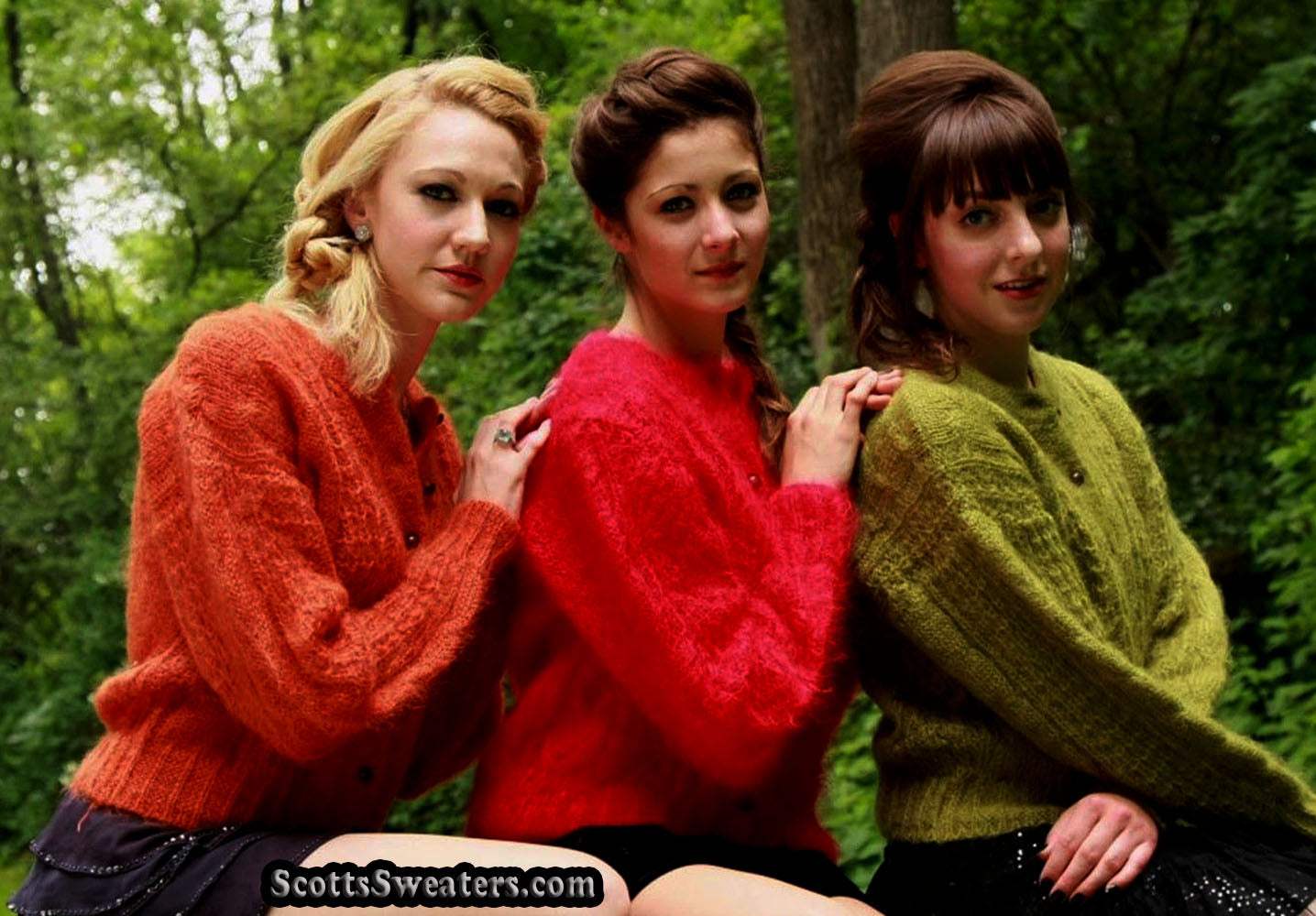 Three women wearing retro Italian cable-knit mohair cardigan sweaters in orange, red, and green outdoors