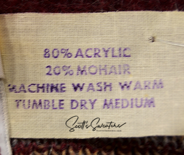 Close-up of a fabric care label on a Retro Shaggy Argyle mohair sweater showing 80% acrylic, 20% mohair, machine wash warm, and tumble dry medium instructions.