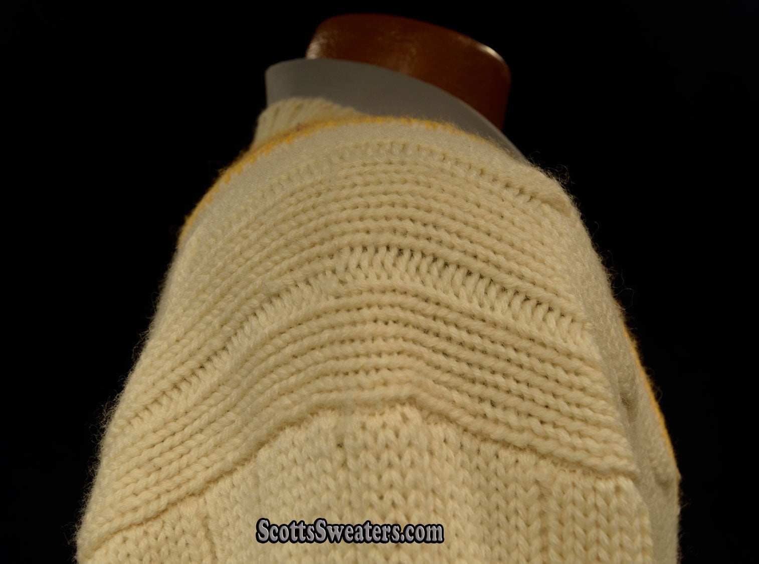 Ivory cable-knit wool tennis sweater with yellow, blue, and red striped neckline on mannequin