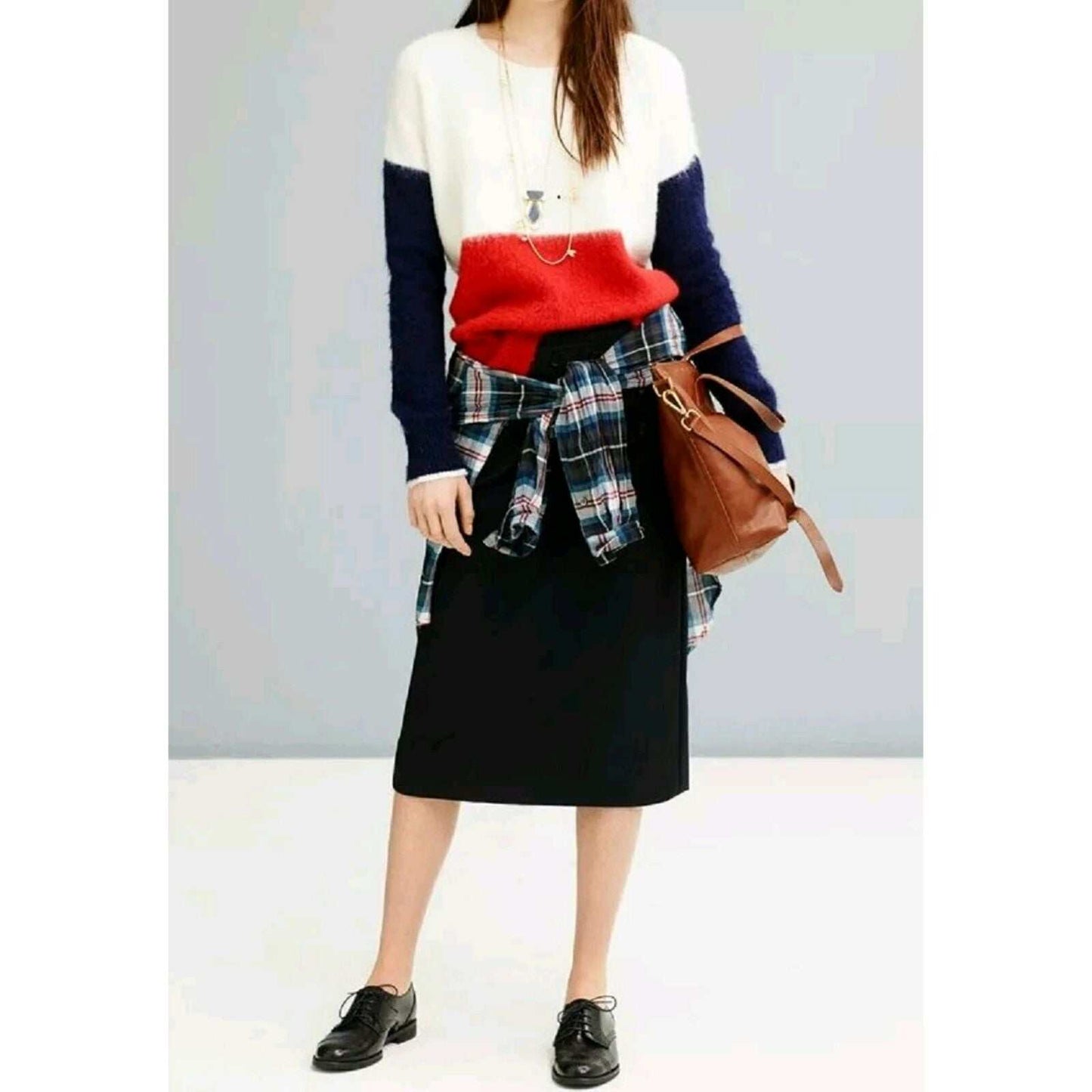 Woman wearing a white, red, and navy color-block mohair sweater with a black skirt, plaid shirt tied around the waist, black shoes, and brown handbag