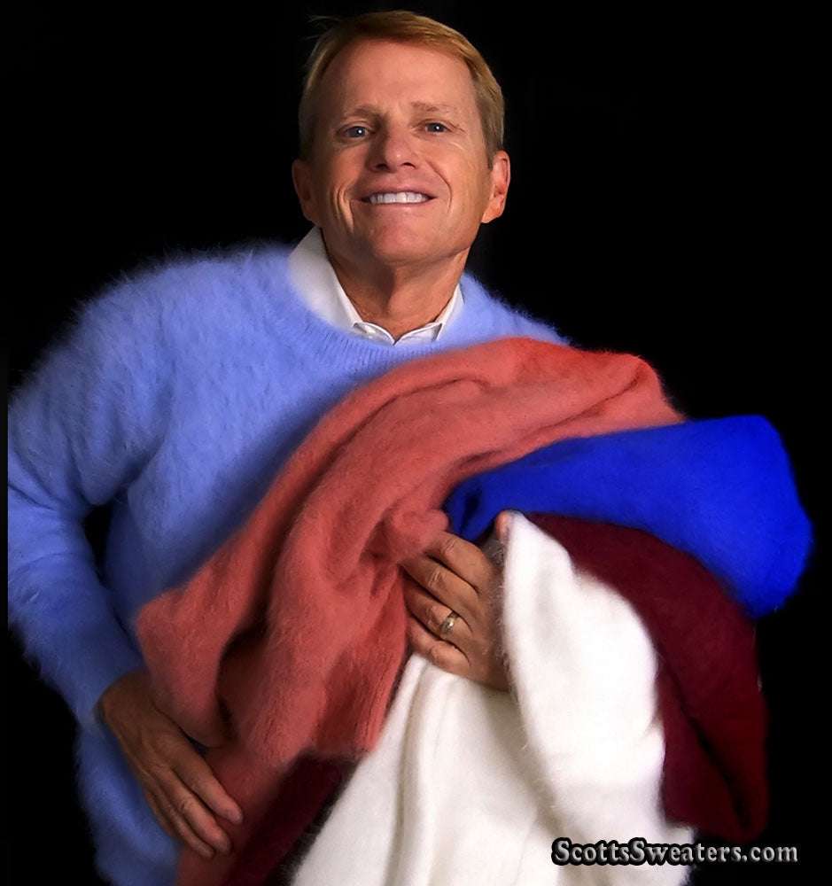 Man wearing light blue ultra-soft angora crewneck sweater holding multiple colorful angora sweaters