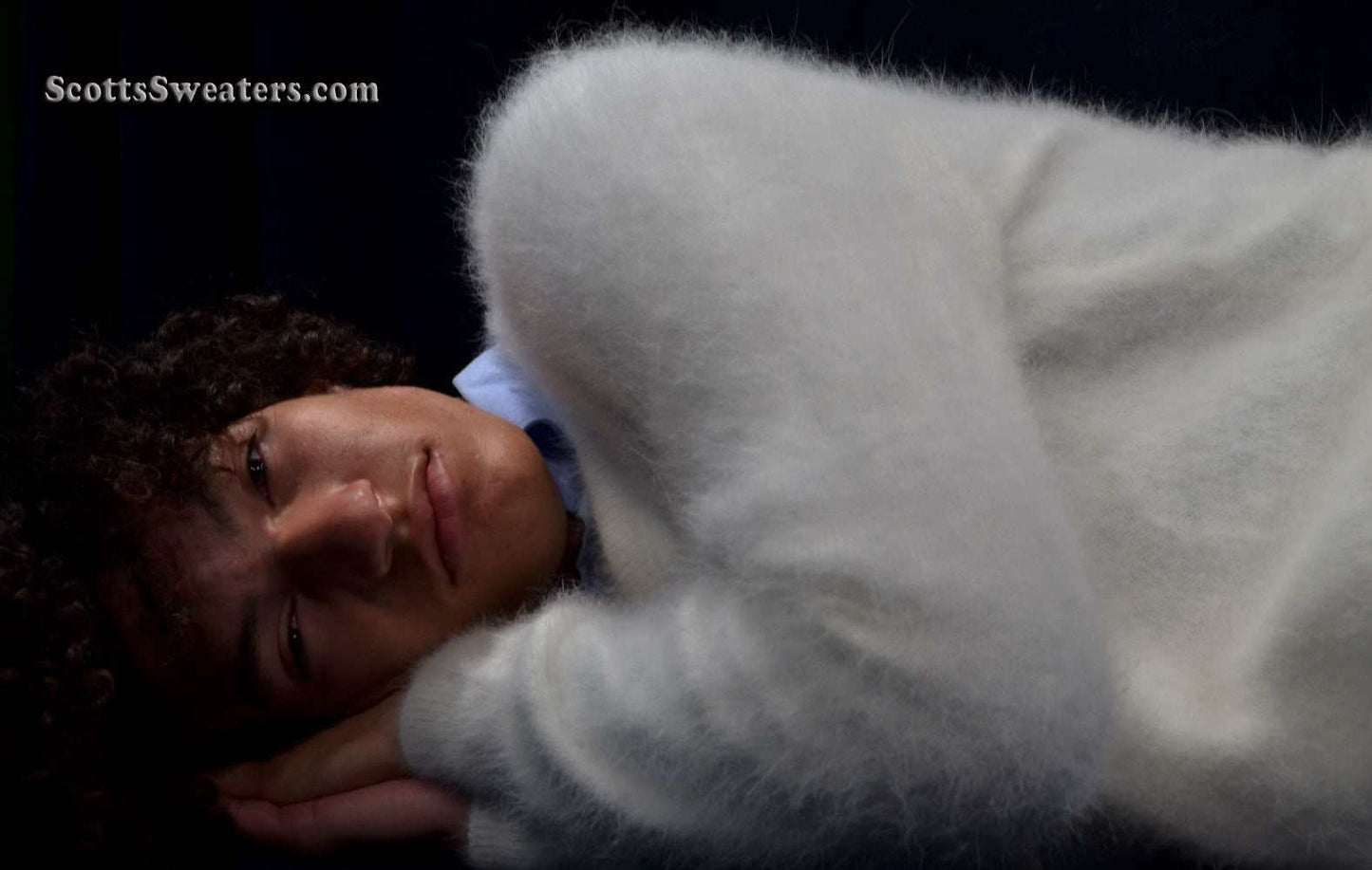 Man wearing a white ultra-soft angora V-neck sweater lying down against a dark background