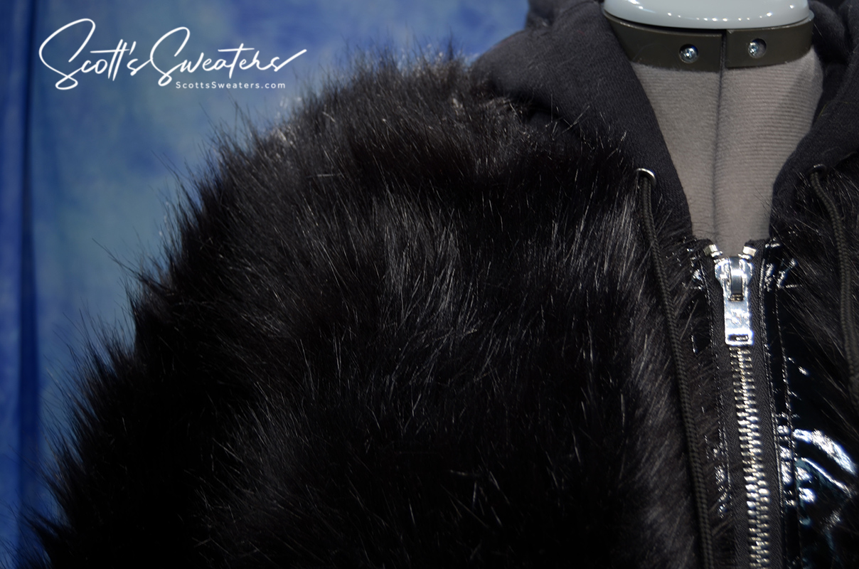 Punk style thick black fluffy faux-fur jacket with zipper front, hood, hanging straps, and metal D-rings on cuffs.