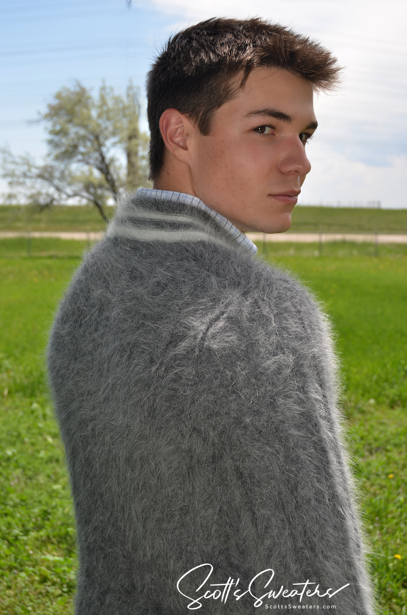 Young man wearing a grey ultra-soft men's angora tennis sweater outdoors in a green field