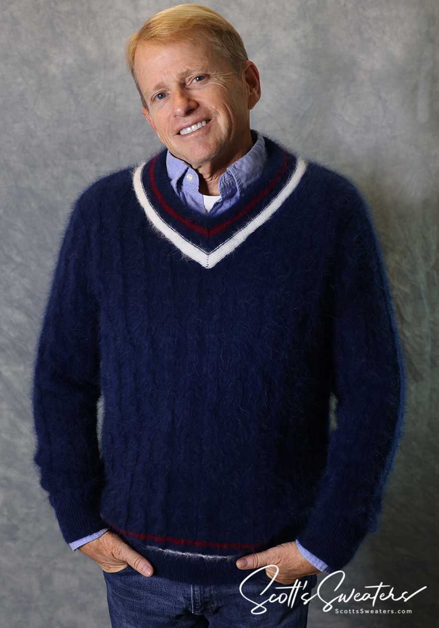 Man wearing a navy blue ultra-soft angora men's tennis sweater with cable knit and V-neck stripes, smiling against a gray backdrop