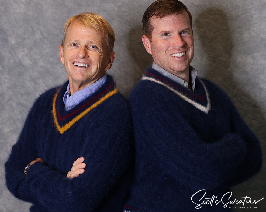 Two men wearing navy blue ultra-soft angora men's tennis sweaters with contrasting V-neck stripes, smiling and posing against a grey backdrop