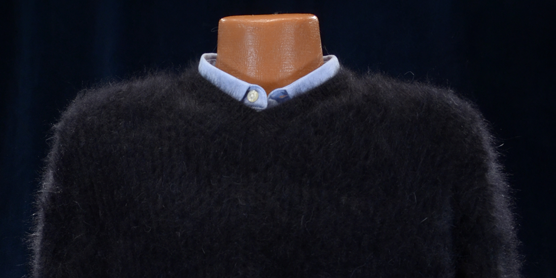 Men's soft luxurious black angora sweater with rib-knit and close-cut V-neck layered over light blue collared shirt on mannequin