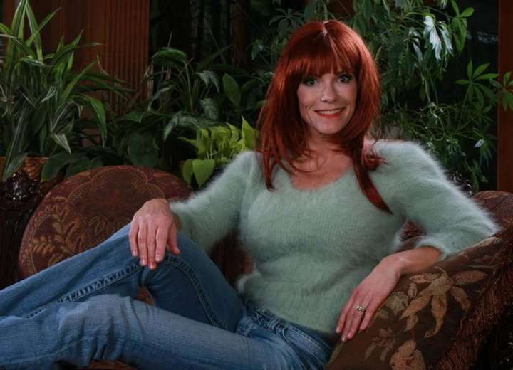 Woman wearing a light green fuzzy angora cropped 3/4-sleeve sweater with V-neck and blue jeans sitting on a patterned chair.