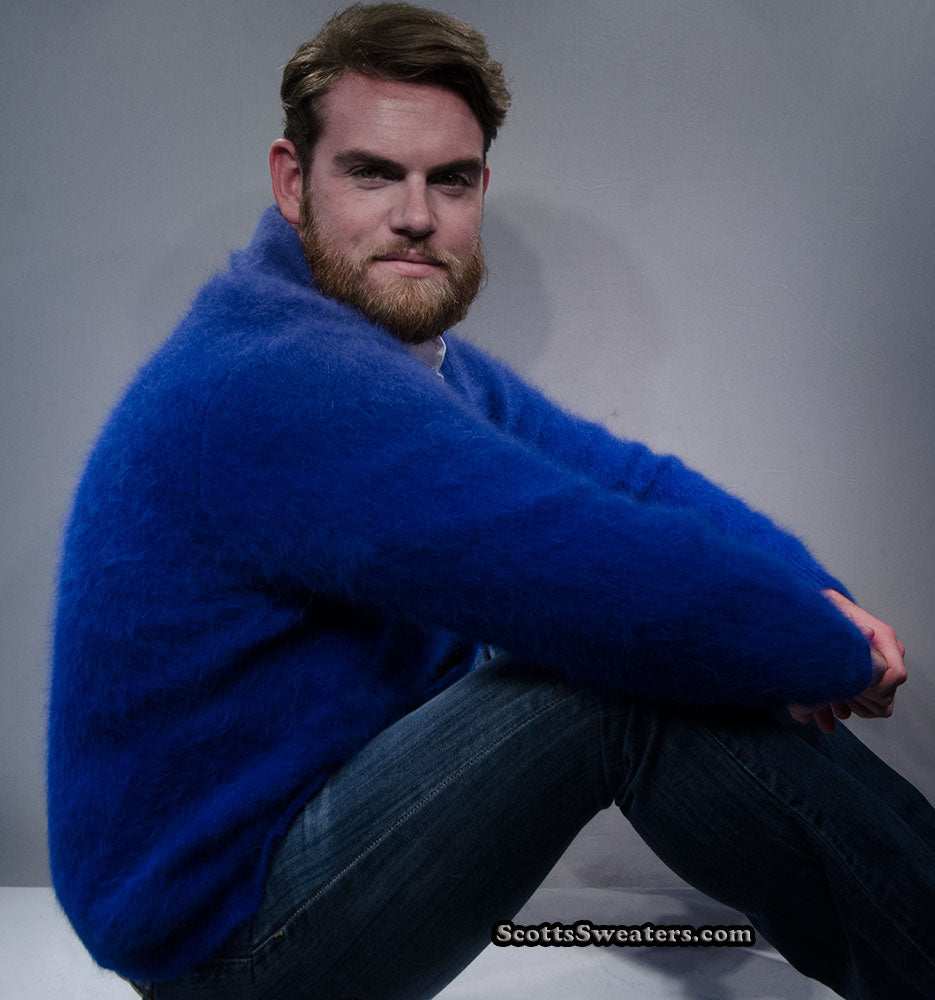 Man wearing royal-blue men's solid-color angora cardigan sweater with shawl-neck collar sitting against gray background