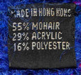 Close-up of black fabric label on blue speckled mohair sweater showing 55% mohair, 29% acrylic, 16% polyester content.