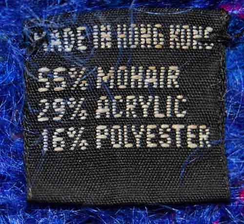 Close-up of black fabric label on blue speckled mohair sweater showing 55% mohair, 29% acrylic, 16% polyester content.