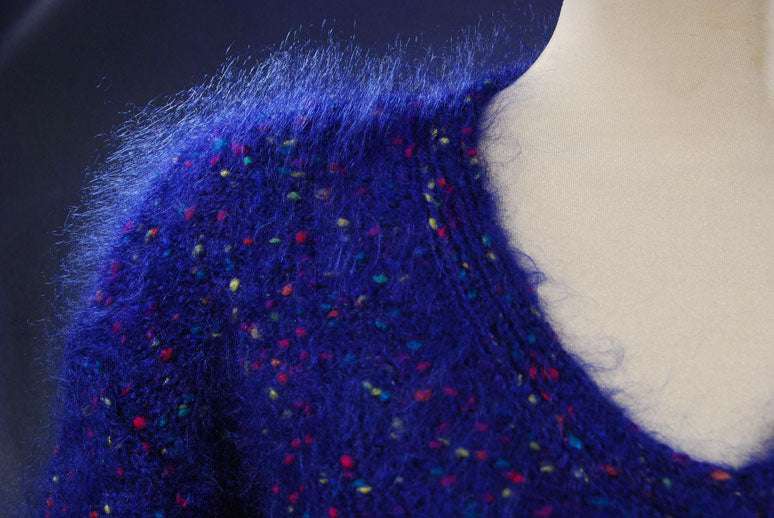 Close-up of woman's blue speckled mohair V-neck sweater with multicolored knit-in specks