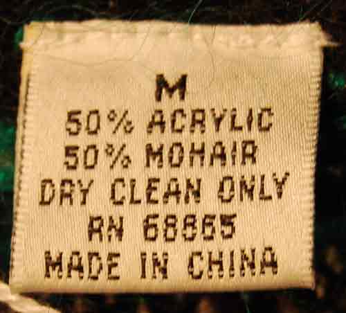 Close-up of a clothing tag showing fabric composition 50% acrylic and 50% mohair, size medium, dry clean only, made in China for a woman's black multi-color striped crewneck mohair sweater.