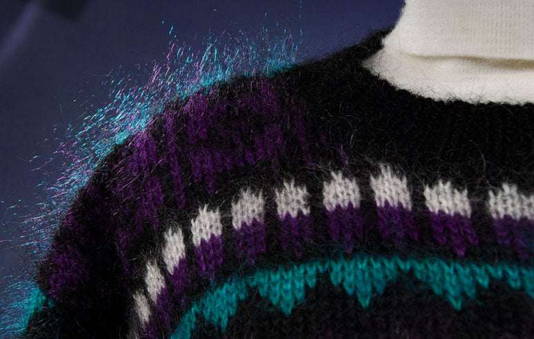 Close-up of woman's black multi-color striped mohair crewneck sweater with purple, white, and teal patterns