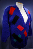 Woman's colorful deep V-neck jewel-tone sweater with red, black, and green geometric design by Nell Flowers