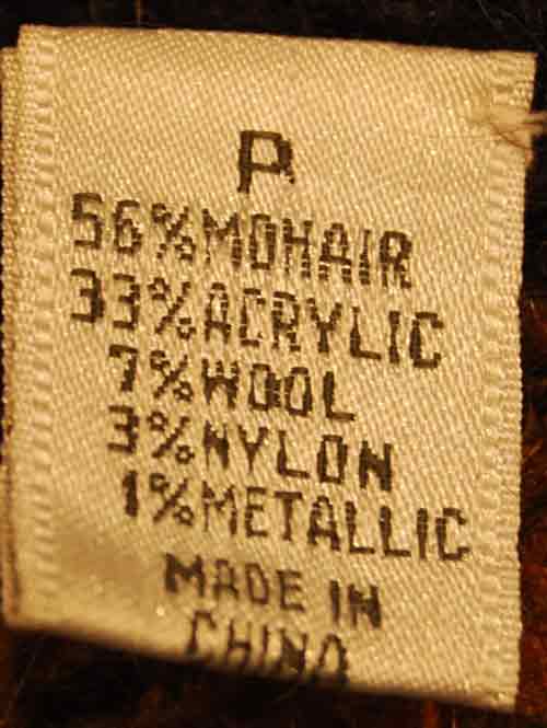 Label showing fabric composition of woman's long black cardigan mohair sweater with metallic gold crest design
