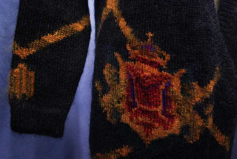 Close-up of woman's long black mohair cardigan with metallic gold and red crest design on sleeve and front panel