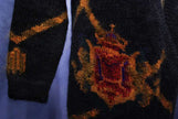 Close-up of woman's long black mohair cardigan with metallic gold and red crest design on sleeve and front panel