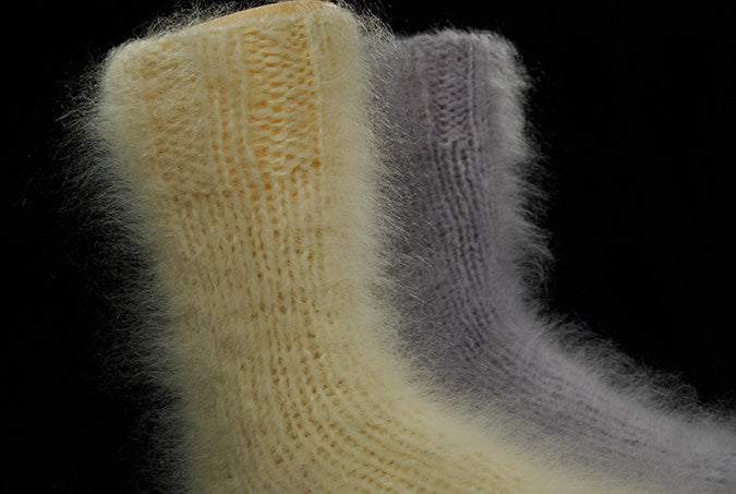 Hand-knit thick warm mohair socks in soft yellow and gray colors against black background