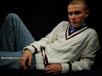 Men's classic V-neck cable-knit white tennis sweater with maroon trim modeled by a man reclining against black background