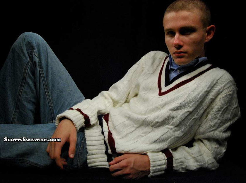 Men's classic V-neck cable-knit white tennis sweater with maroon trim modeled by a man reclining against black background