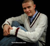 Men's classic V-neck cable-knit tennis sweater in white with maroon stripes, worn by smiling man sitting cross-legged