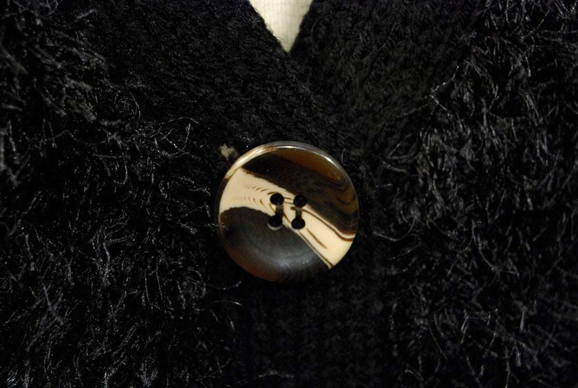 Close-up of black woman's eyelash cardigan sweater with shiny four-hole button and fuzzy acrylic fibers resembling rabbit fur
