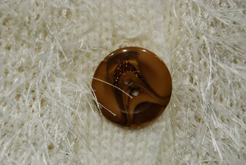 Close-up of brown button on white fuzzy eyelash cardigan sweater with long acrylic fibers