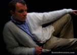 Man wearing men's ultra-soft angora white cardigan sweater with blue shirt and beige pants against black background