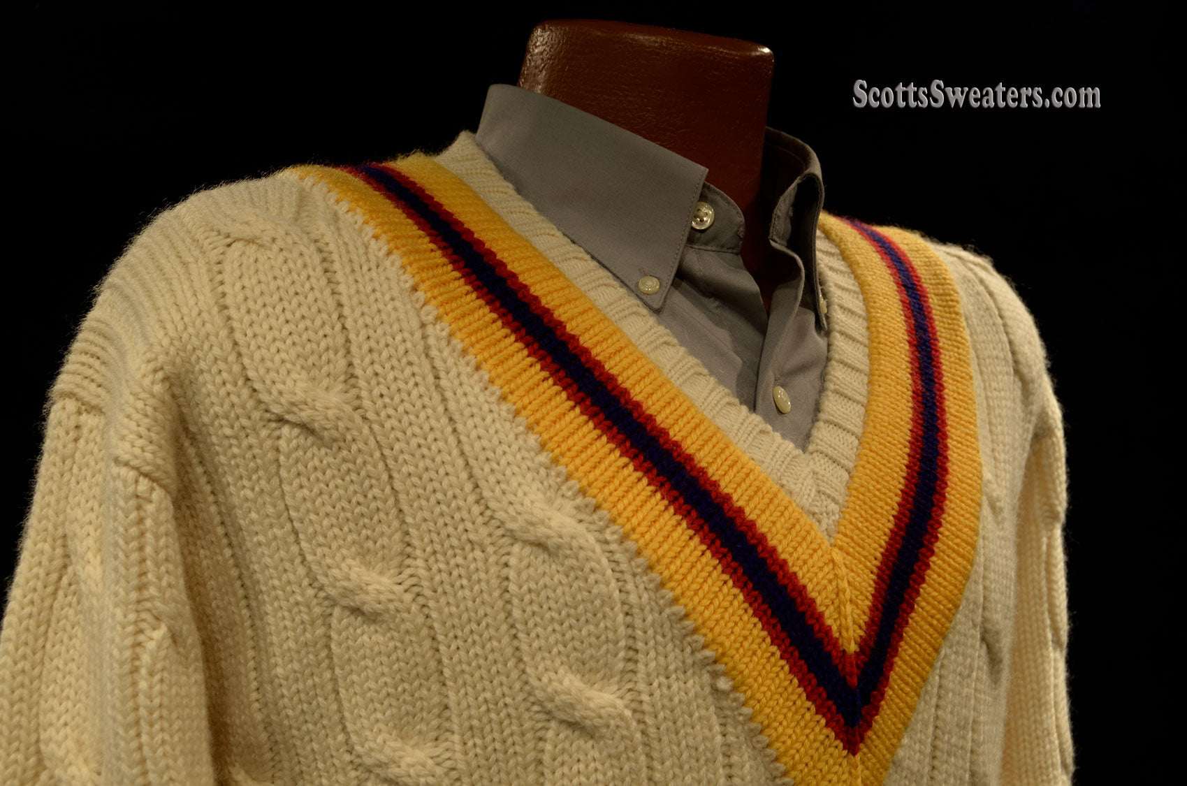 Ivory wool cable-knit tennis sweater with yellow, blue, and red striped V-neck collar.
