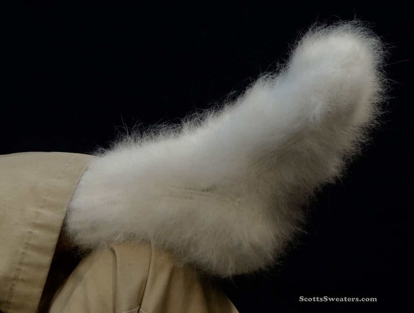 White hand-knit Siberian Angora socks, thick and warm, worn on a foot against a black background