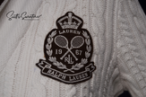 Close-up of Woman's white cable-knit cardigan showing Ralph Lauren tennis crest patch