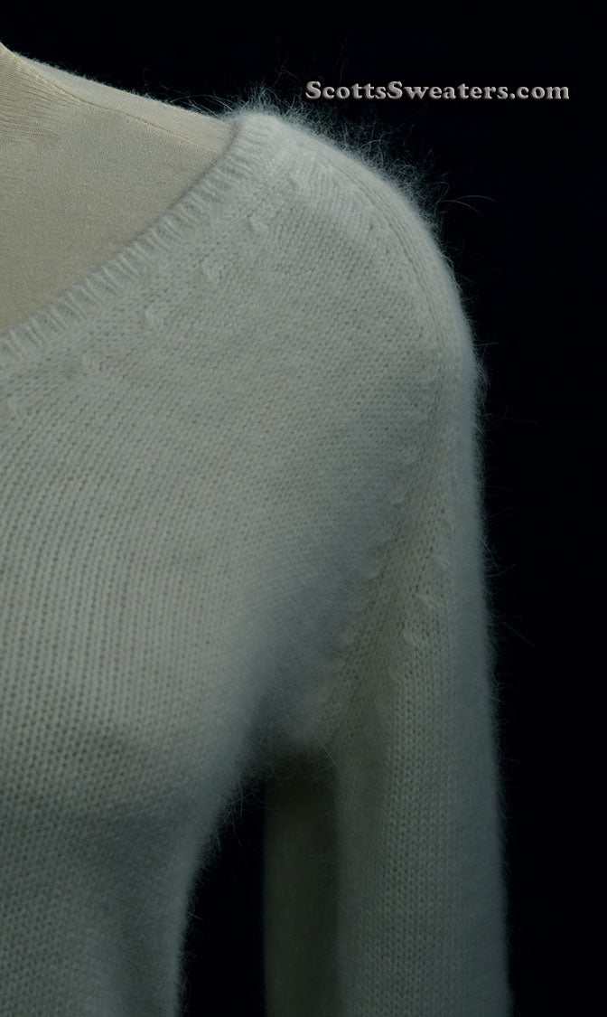 Close-up of woman's white angora V-neck sweater with soft texture and split cuffs detail
