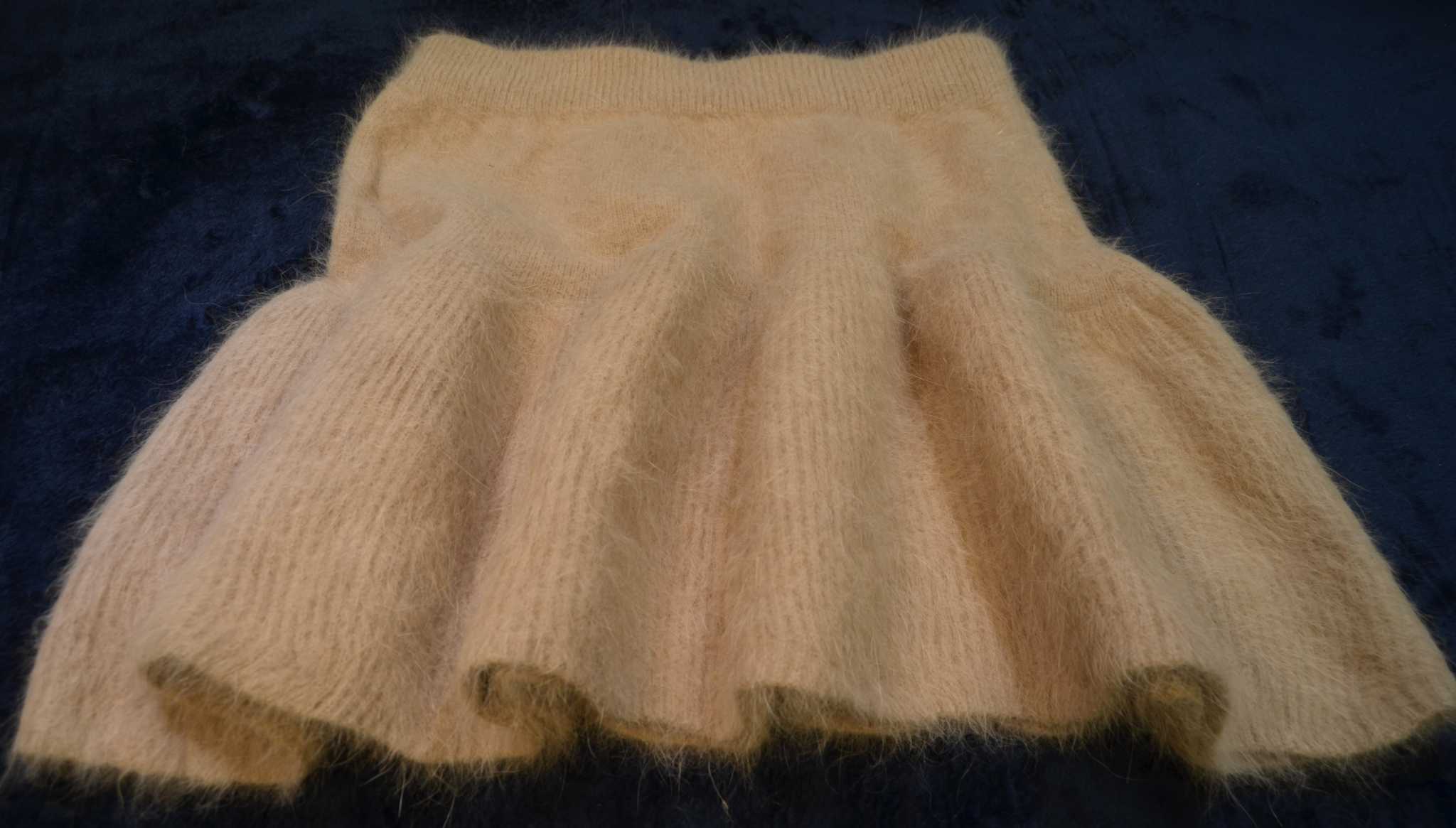 Soft beige woman's short angora skirt with elastic waistband on dark background